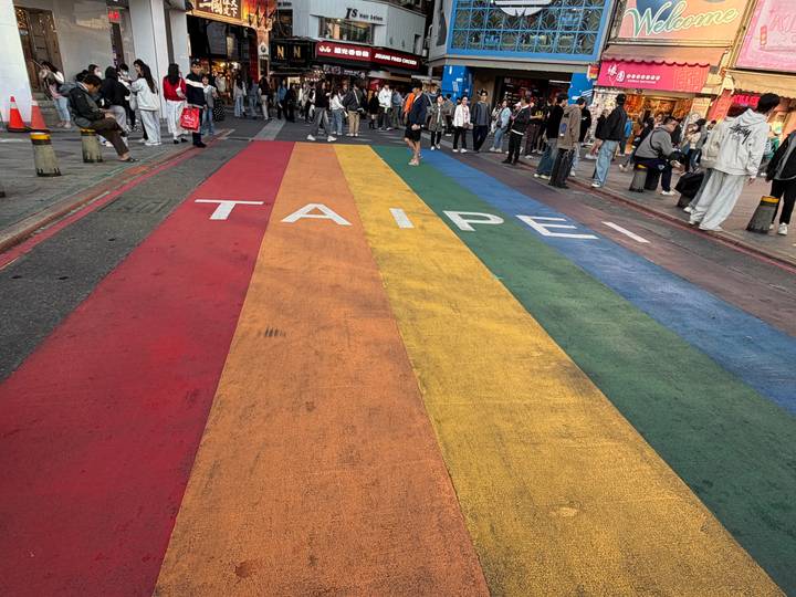 Crowds walk across a rainbow-painted pedestrian crossing emblazoned with 'TAIPEI'.