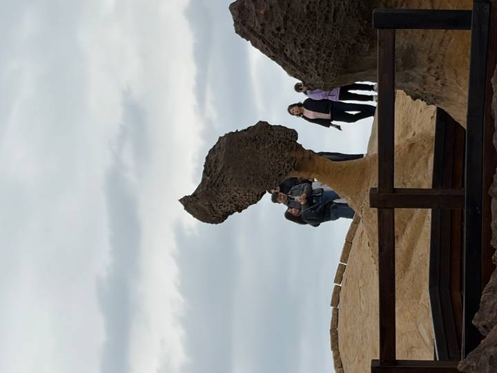 Visitors pose beside the famous Queen's Head rock formation under an overcast sky.