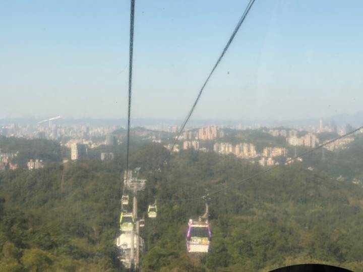 Blurred view through gondola glass of Taipei city and forested hills below suspension cables.