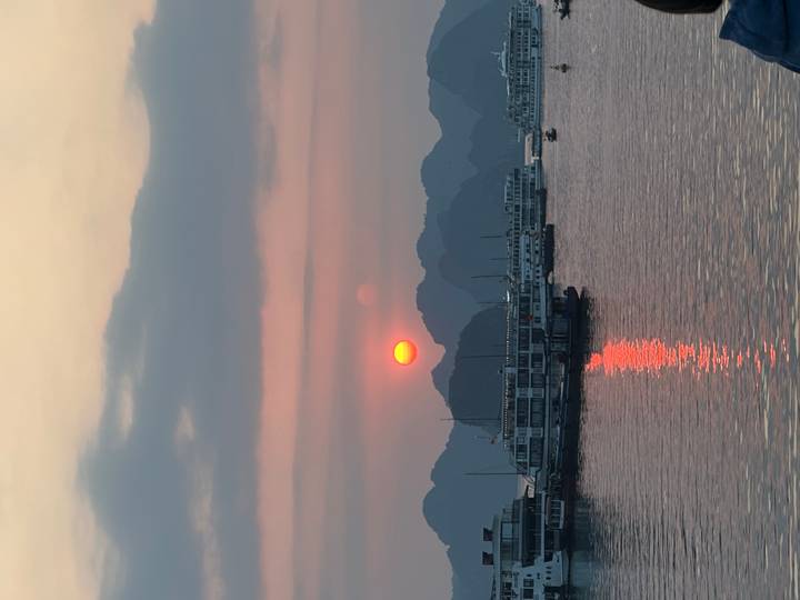 Orange sun setting behind limestone karsts with cruise boats reflecting on Halong Bay.