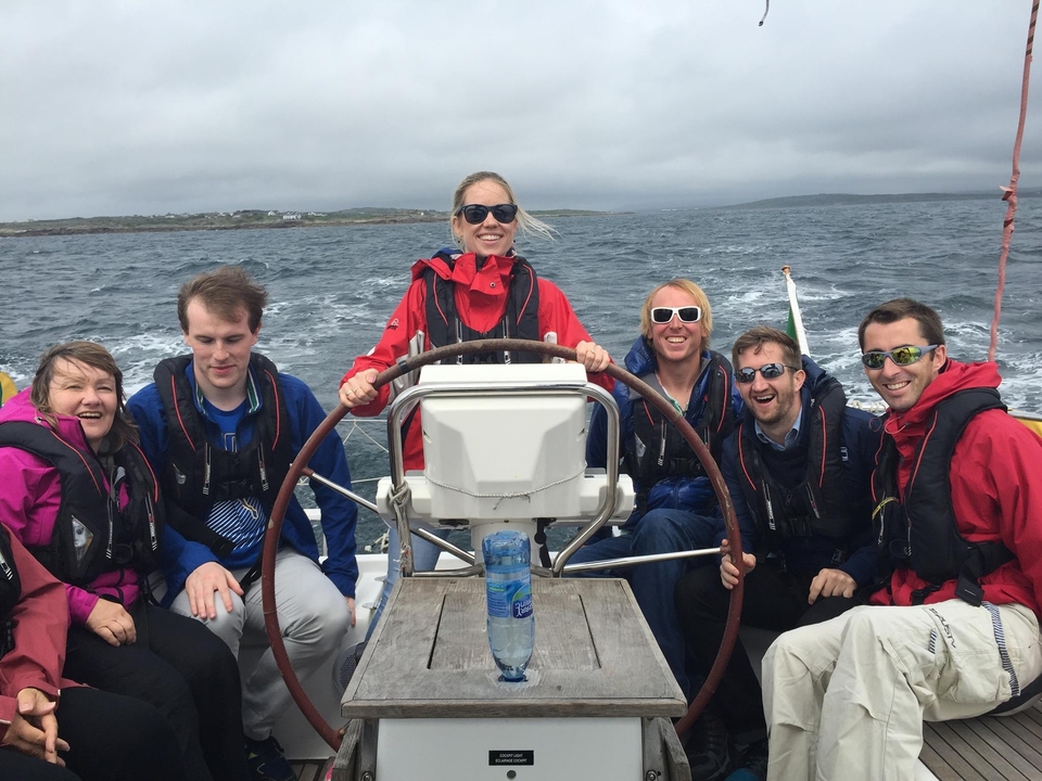 Groupe de personnes sur un bateau, souriantes, par une journée nuageuse.