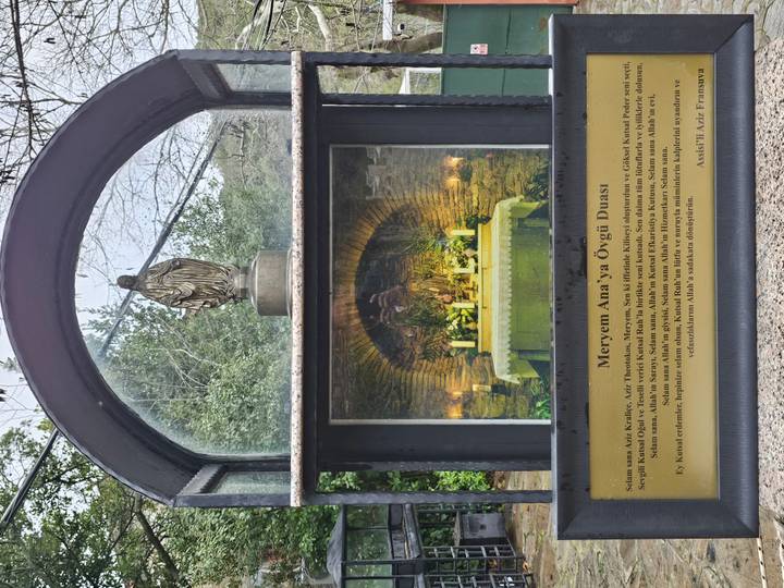 Informational shrine display with statue of Mary and Turkish prayer text set into a stone niche.