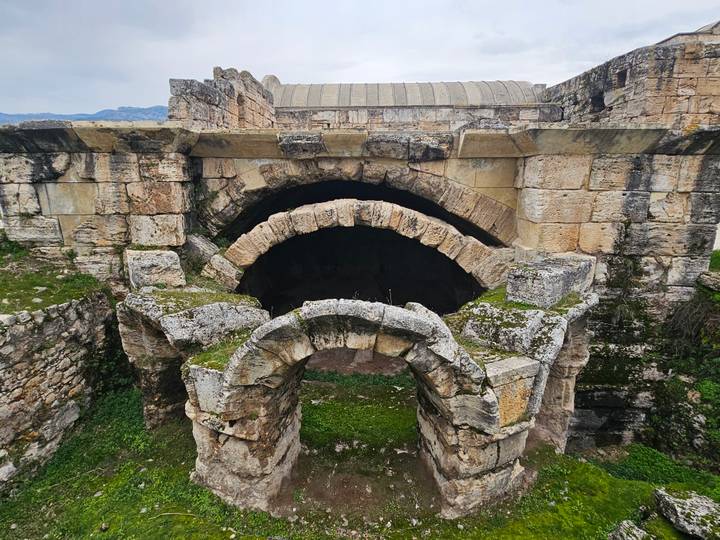 Moss-covered stone arches and vaults of an ancient Roman bath complex amid grassy ruins.
