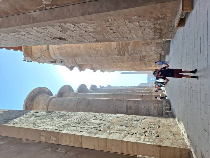 Visitors walking between towering stone columns toward an obelisk in Karnak Temple complex