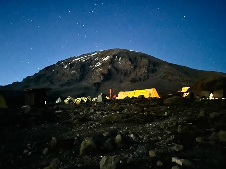 Night view of illuminated tents under a starry sky at the base of Mount Kilimanjaro