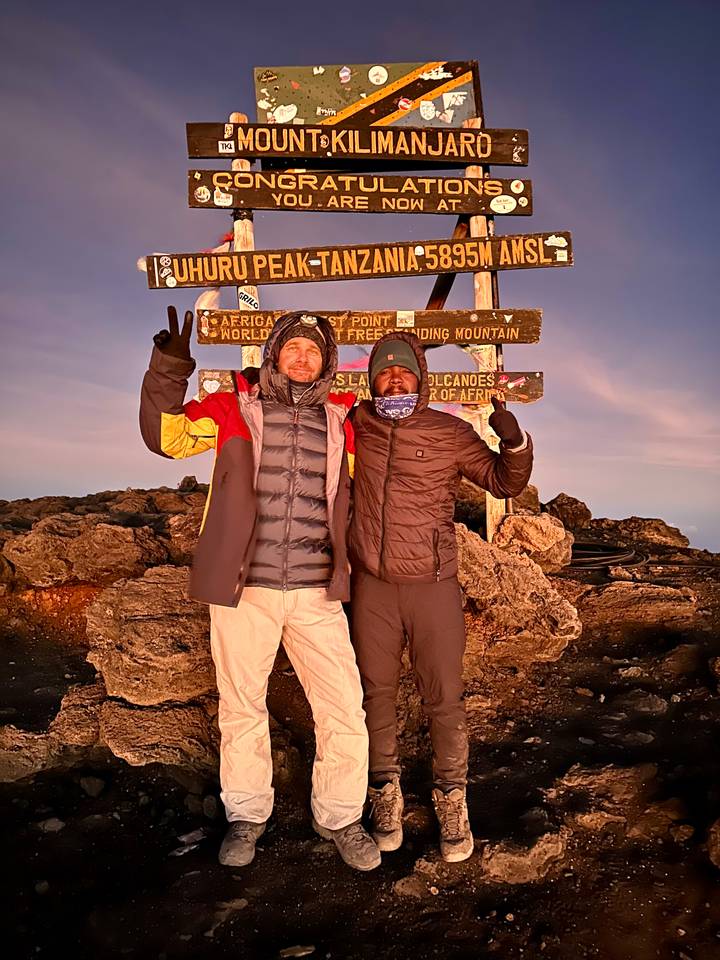 Two climbers posing with summit sign at sunrise on Mount Kilimanjaro
