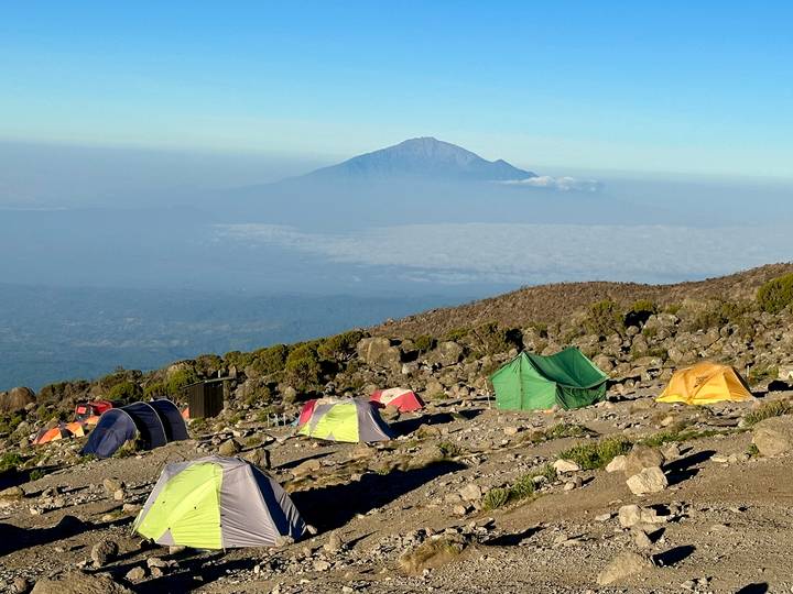 Colorful tents scattered on a rocky alpine plateau with a distant volcanic peak rising above the plains.