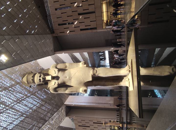 Colossal statue of Ramses II inside the Grand Egyptian Museum hall with visitors lining the base.