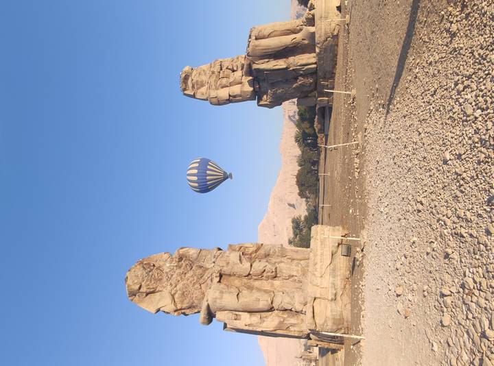 Hot-air balloon floating between the Colossi of Memnon in the early morning light.