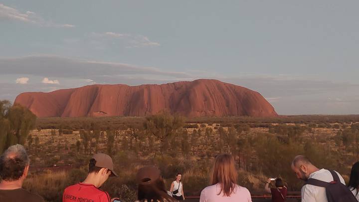 Tourists gathered at a viewpoint watching Uluru glow in the evening light