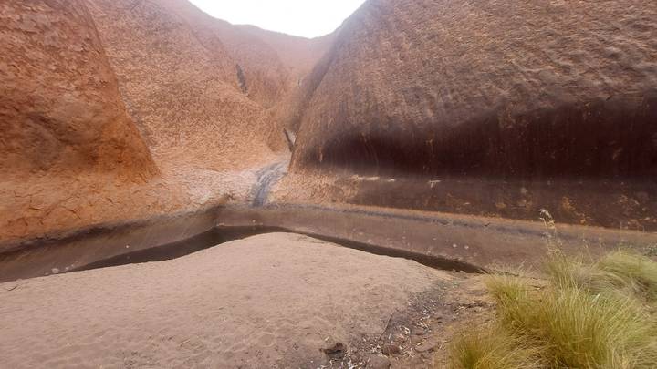 Shallow waterhole nestled between towering rust-red rock walls at Uluru