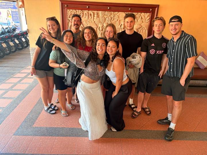 Smiling group of young travelers pose for a photo indoors before scooters lined up outside.