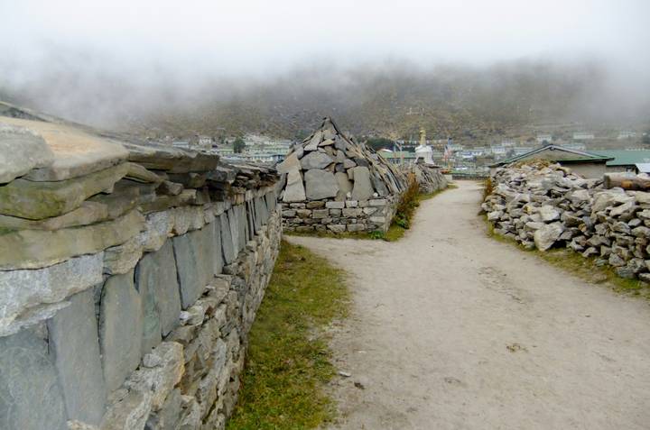 Misty mountain village lane flanked by stone Mani walls and prayer slabs on the Everest trail.