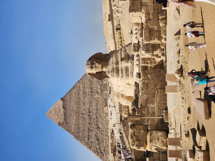 Iconic view of the Sphinx with the Pyramid of Khafre towering behind and visitors below.