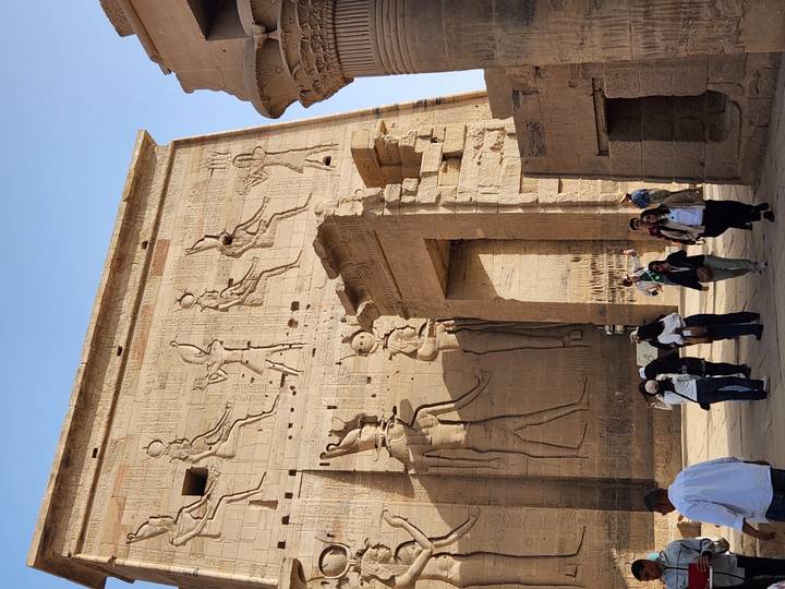 Travelers entering the monumental pylon richly carved with Egyptian deities at Edfu Temple.