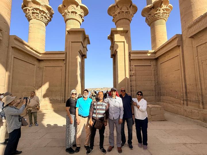 Tour group posing between tall sandstone columns of an ancient Egyptian temple under clear skies.