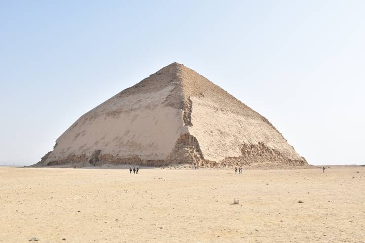 The Bent Pyramid stands isolated in the desert with a pale sky backdrop.