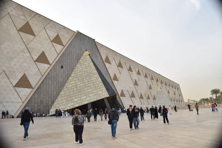 Facade of the new Grand Egyptian Museum with pyramid-shaped entrance and visitors outside.