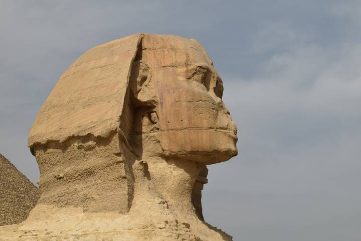 Profile view of the Great Sphinx head and shoulders against a partly cloudy sky.