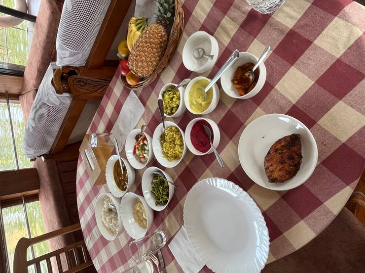 A checked tablecloth holds an inviting South Indian meal with assorted curries, vegetables and chutneys laid out on a houseboat dining table.