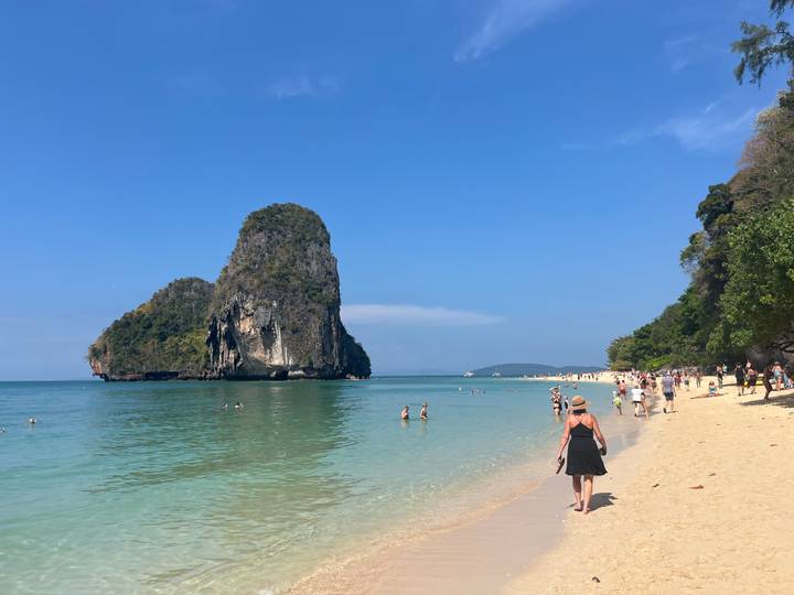 Beachgoers enjoy the clear water and soft sand of Railay with a towering limestone stack offshore.