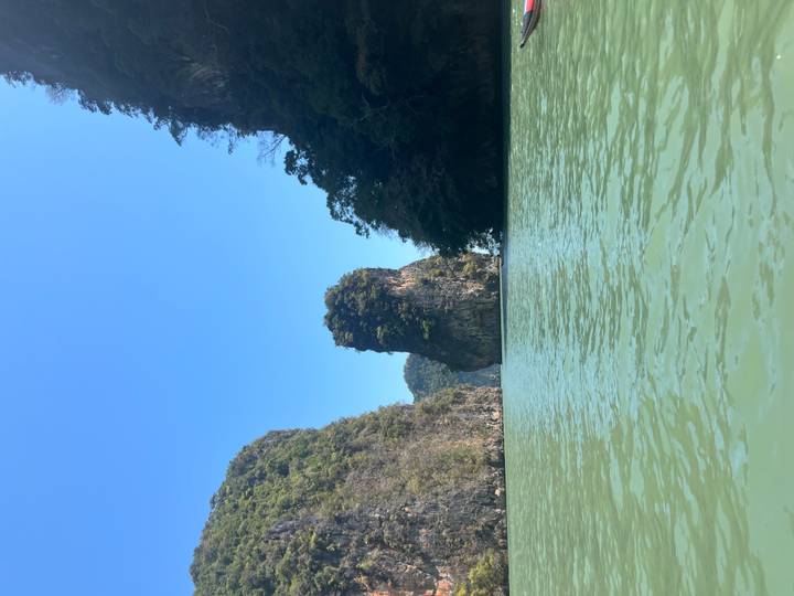 Tall limestone karst island rising from turquoise water under a clear blue sky.