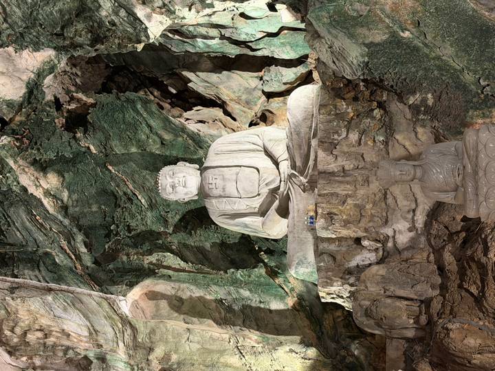 Illuminated Buddha statue carved inside a limestone cave chamber.