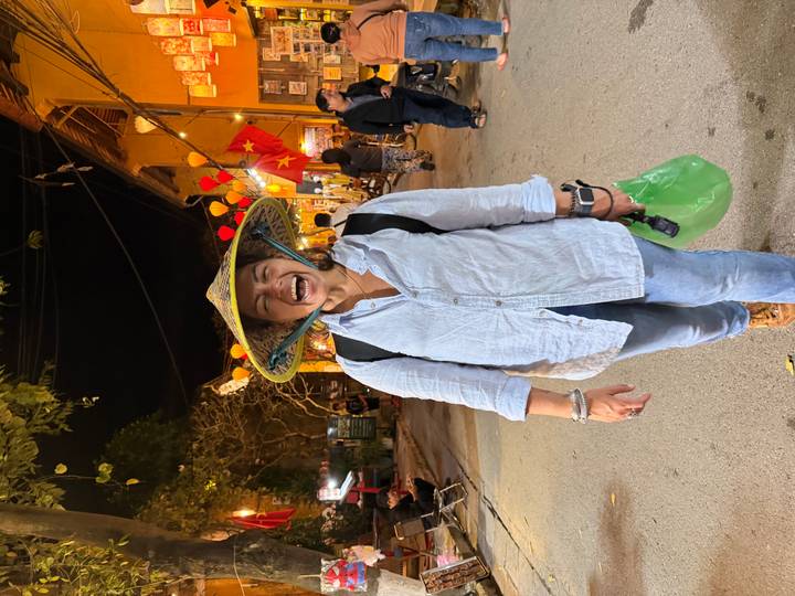 Laughing traveller wearing a conical hat on a lantern-lit street at night.