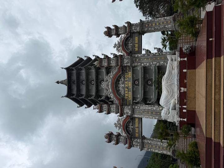 Pagoda complex with reclining white Buddha statue in front of ornate gray tower under cloudy skies.