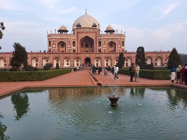 Humayun’s Tomb stands majestically behind a long reflecting pool and gardens with visitors strolling about.