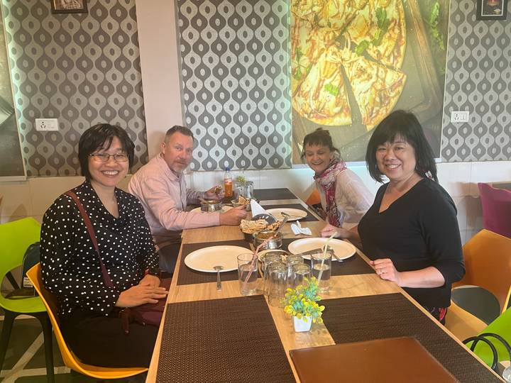 A group of diners sit around a wooden table in a casual restaurant, ready to enjoy an Indian meal.