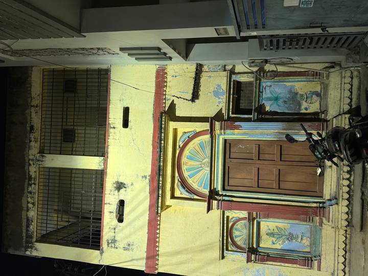 Faded yellow facade of an old building with arched wooden doors and a parked scooter at night.