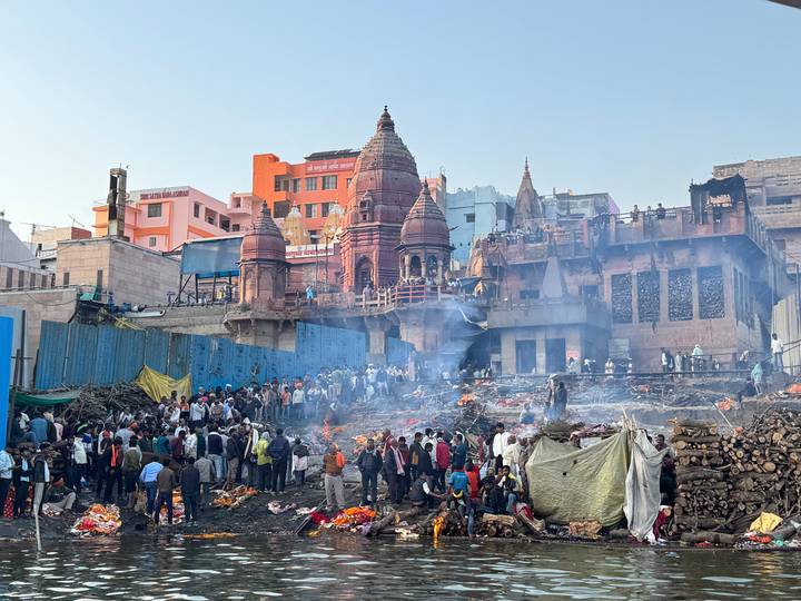Cremation fires burn on the riverbank as crowds gather around historic buildings and temples in Varanasi.