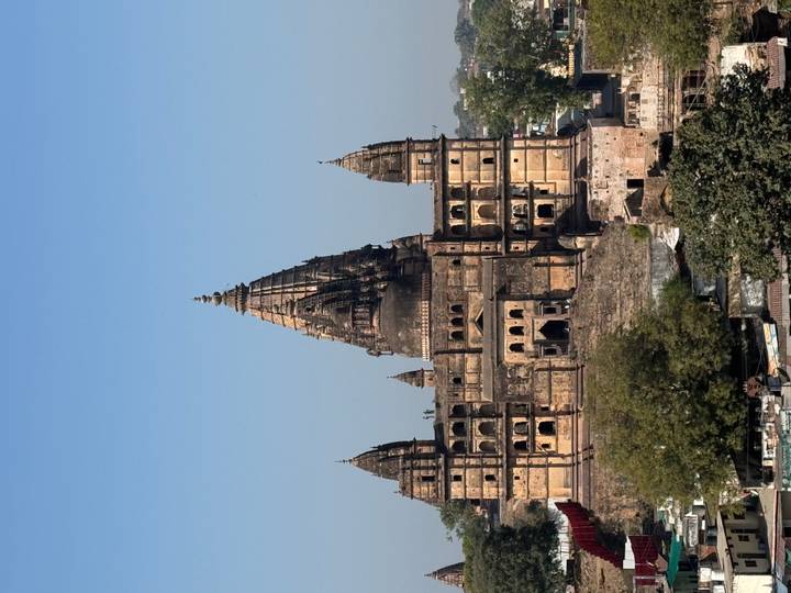 Tall spired medieval temple of Orchha rises above the surrounding town under a clear sky.