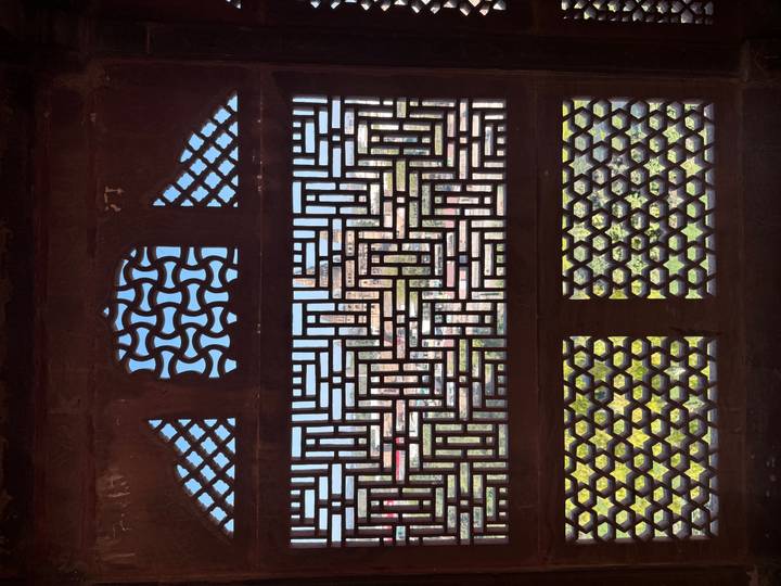 Intricate lattice stone window looks out toward a distant temple and green gardens.