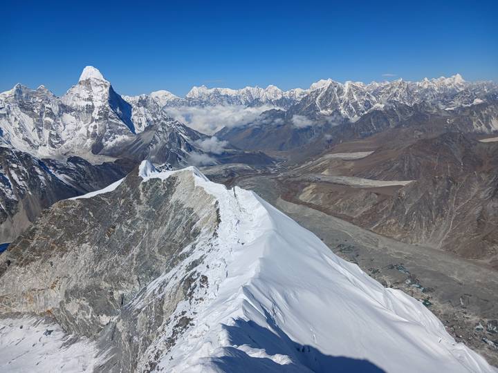 Snow corniced ridge contrasts with immense rocky valleys and snow-clad summits stretching to the horizon.