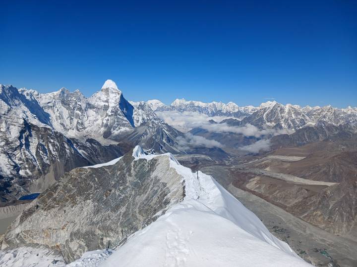 Crystal clear panoramic shot of Himalayan ridge leading to snow pyramids over deep blue sky.