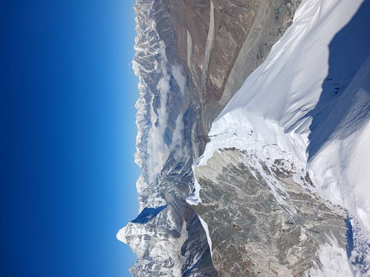 Vertical composition of a snowy knife-edge ridge leading into distant Himalayan ranges beneath deep blue sky.
