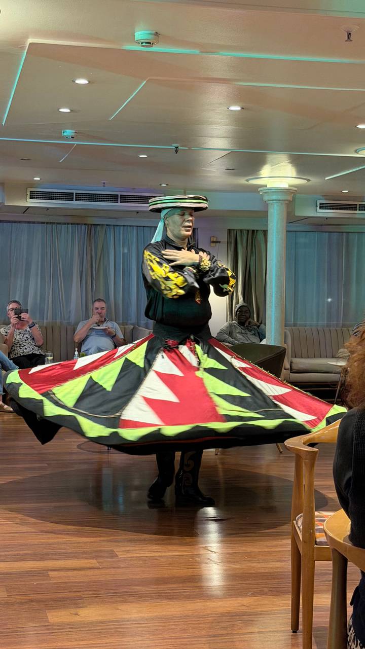 Whirling dervish performer in colourful skirt spins on a Nile cruise stage as seated guests watch.