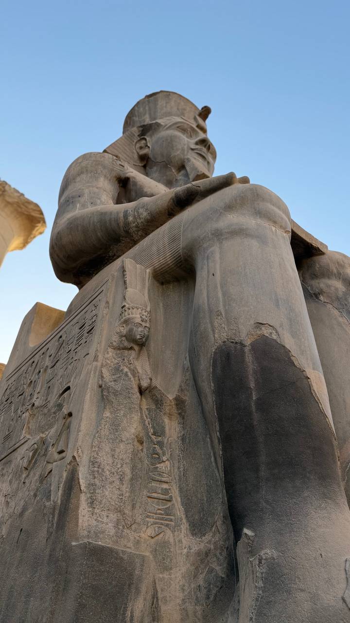 Close detail of a colossal stone statue at an ancient Egyptian temple showing intricate carvings.