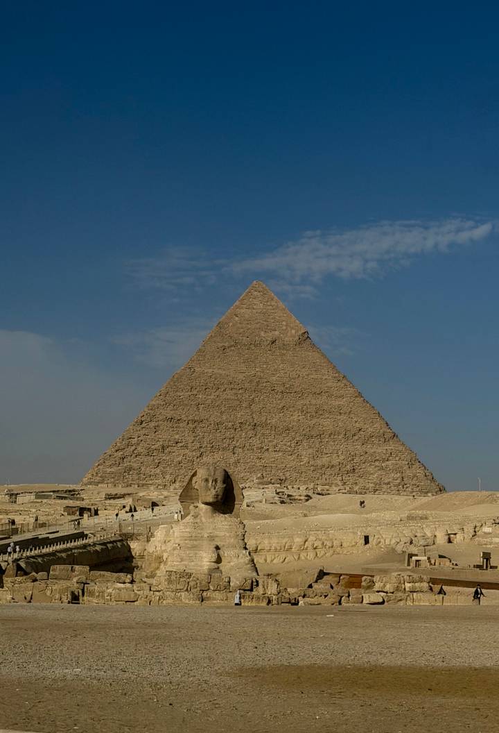 Great Pyramid of Giza rises behind the small Sphinx under a clear sky