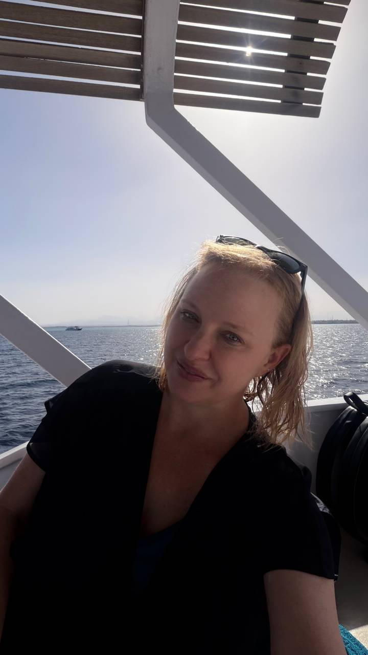 Woman relaxes on boat deck with sparkling sea and distant coastline behind her