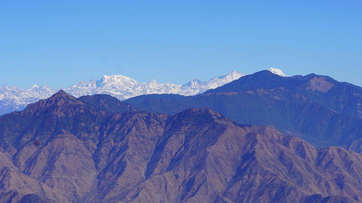 Crisp view of layered brown ridges and distant snow-capped Himalayan peaks under blue sky