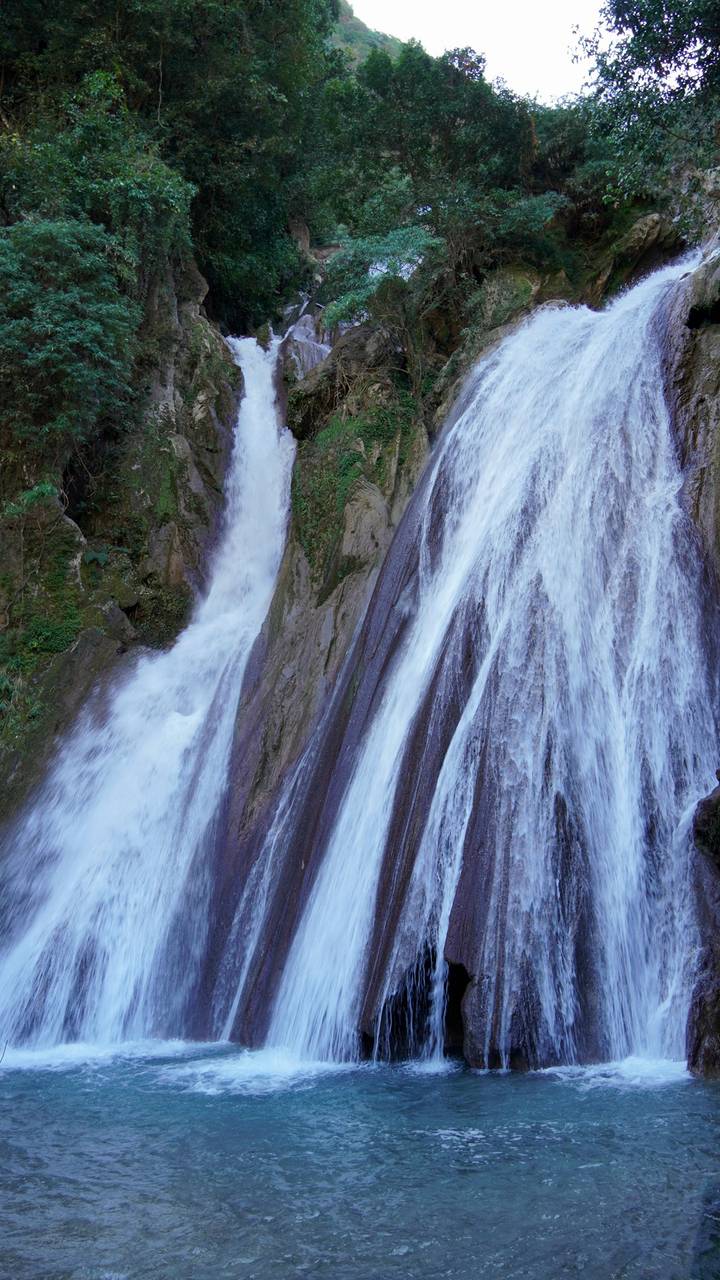 Close-up of twin cascades of a rocky waterfall rushing down lush cliffs