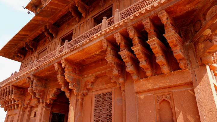 Detailed red sandstone columns and brackets of a Mughal palace bathed in warm light