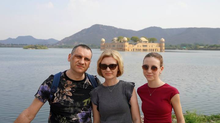 Family standing by the lake with Jal Mahal and surrounding hills in the background