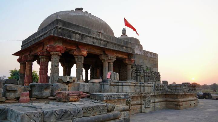Ancient stone temple with red flag atop silhouetted against a hazy sunset sky