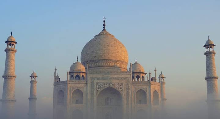 The iconic Taj Mahal rising through early-morning mist with soft golden light