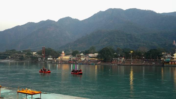 Inflatable rafts on the turquoise Ganges River with Himalayan foothills and a riverside town beyond