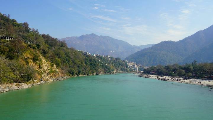 Aqua-blue Ganges flowing through a steep wooded valley beneath a bright sky
